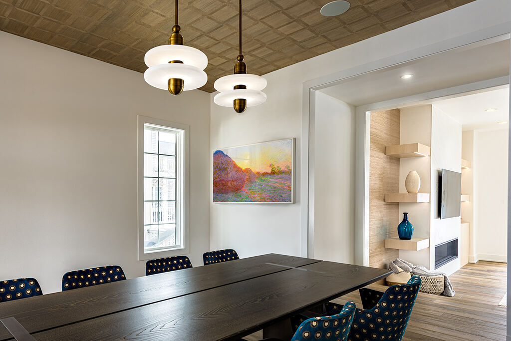 Dining room with a long dark table, patterned chairs, pendant lights, and an opening to the living area