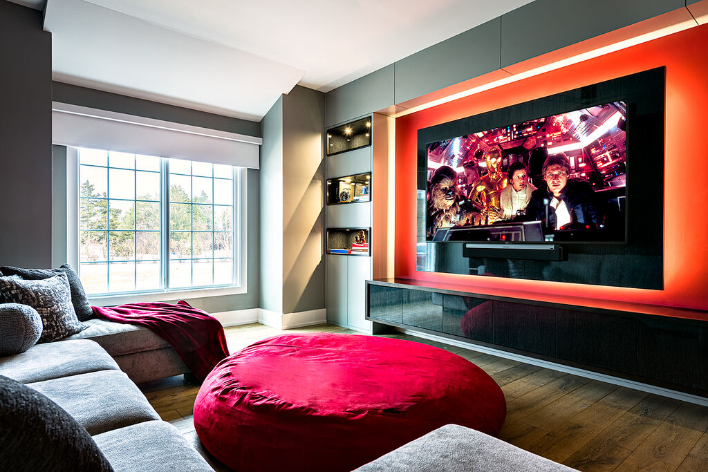 Media room with a wall-mounted display, soundbar, built-in shelving, and red-lit media wall