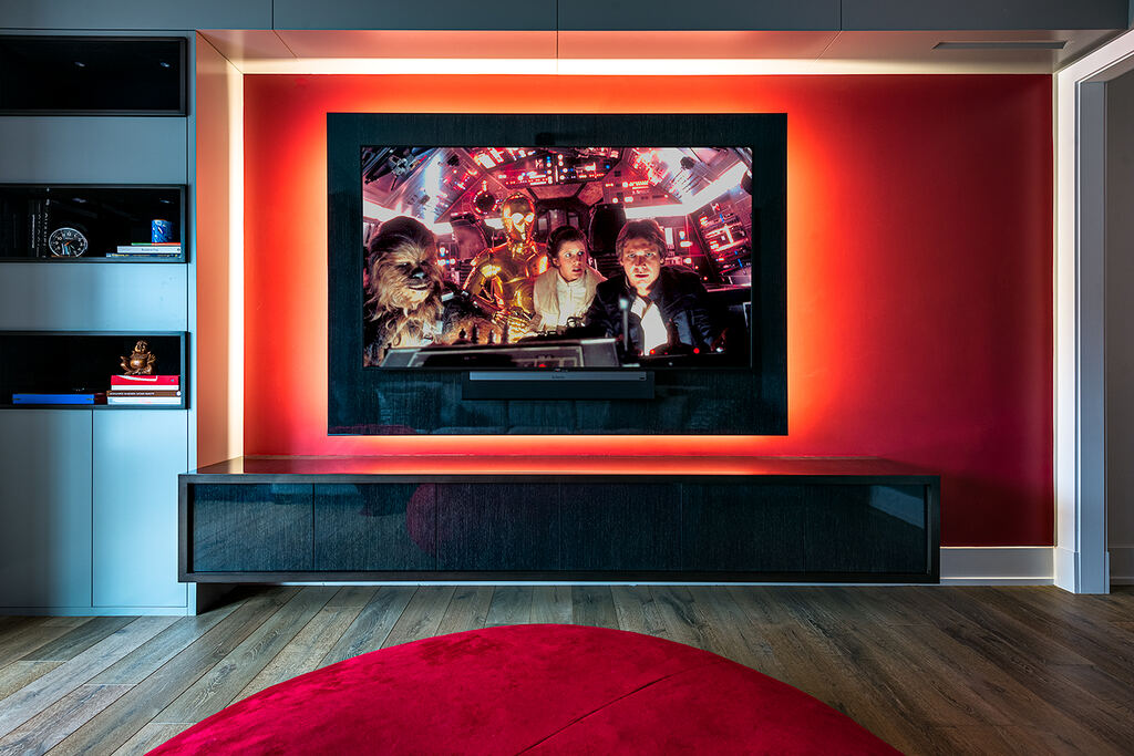 Wall-mounted display and soundbar centered in a red-accented media wall above a low cabinet
