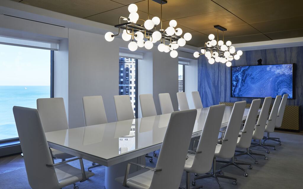Boardroom with a long glass table, display wall, and sculptural ceiling lights